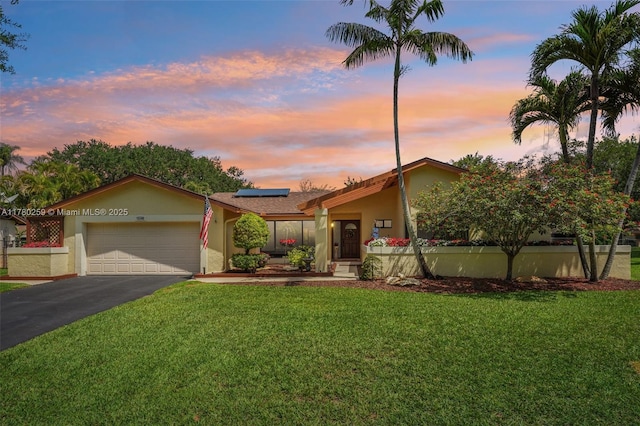 view of front facade with driveway, solar panels, a lawn, and stucco siding