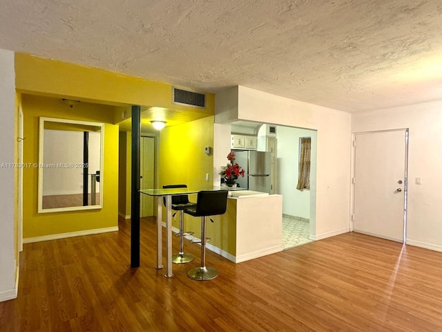 kitchen with a textured ceiling, wood finished floors, freestanding refrigerator, and visible vents