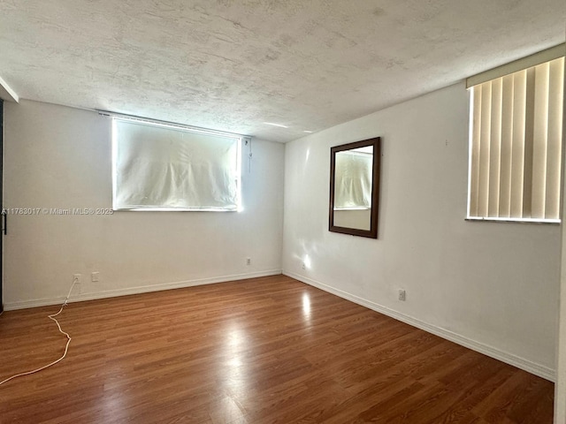 empty room featuring a textured ceiling, wood finished floors, and baseboards