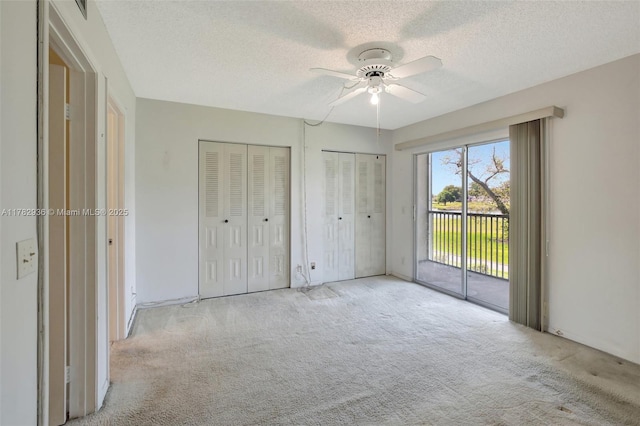 unfurnished bedroom with access to outside, multiple closets, carpet, and a textured ceiling