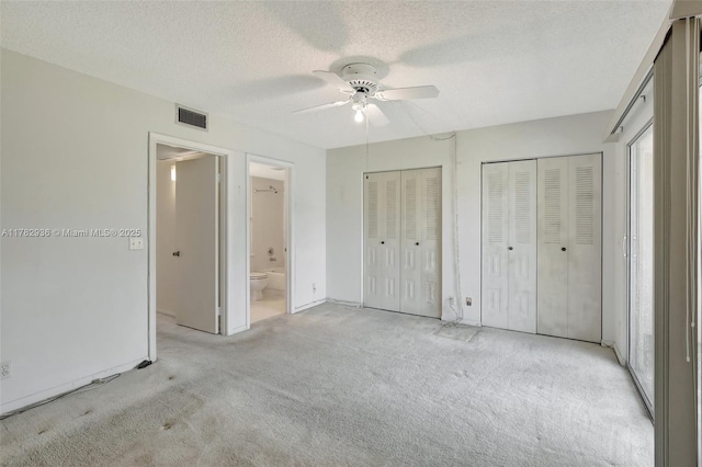 unfurnished bedroom with visible vents, ensuite bathroom, a textured ceiling, carpet floors, and multiple closets