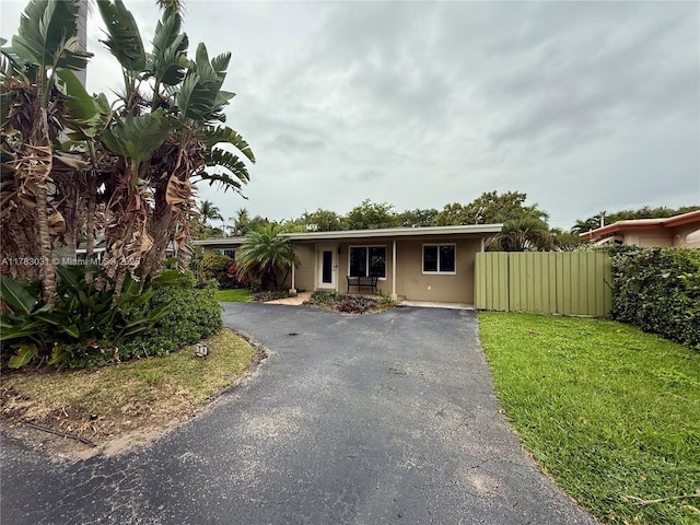 ranch-style home featuring driveway, fence, stucco siding, and a front lawn