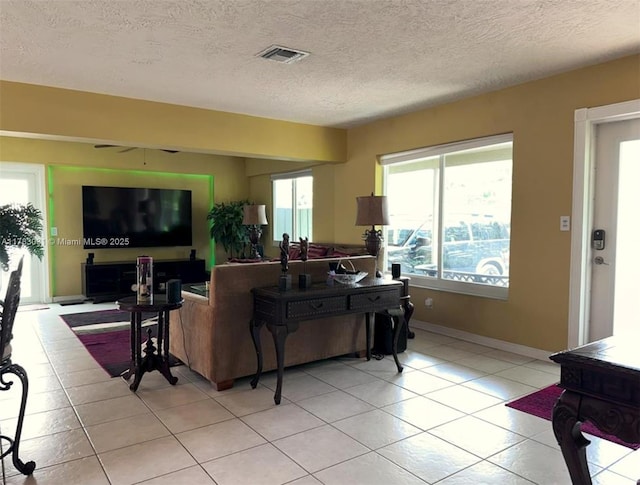living area featuring a textured ceiling, light tile patterned floors, ceiling fan, and visible vents