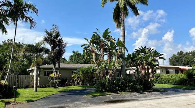 view of property hidden behind natural elements with a front yard and fence