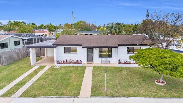 ranch-style house with fence, a front lawn, driveway, an attached carport, and roof with shingles