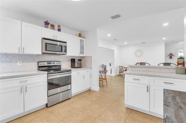 kitchen featuring white cabinets, stainless steel appliances, light tile patterned flooring, visible vents, and decorative backsplash