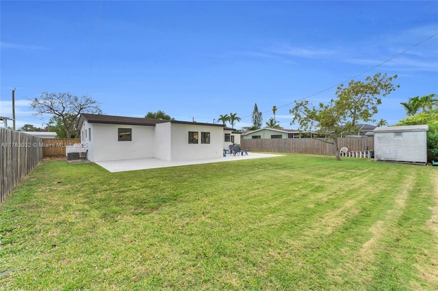 back of property with a fenced backyard, a yard, stucco siding, a patio, and a storage unit