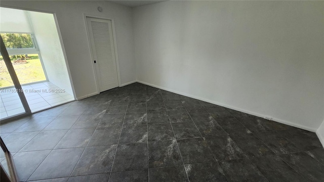 spare room featuring dark tile patterned floors and baseboards