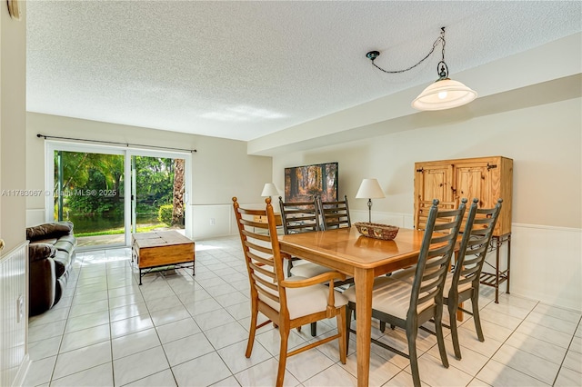 dining room featuring a wainscoted wall, light tile patterned flooring, and a textured ceiling