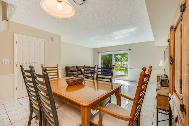 dining room featuring light tile patterned flooring, wainscoting, and a textured ceiling