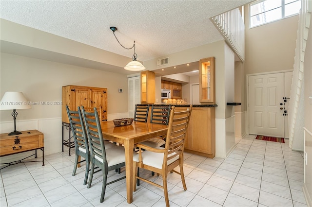 dining area with light tile patterned floors, visible vents, a textured ceiling, and a wainscoted wall