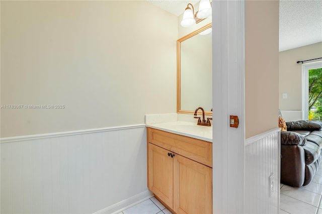 bathroom with a textured ceiling, vanity, tile patterned flooring, and a wainscoted wall