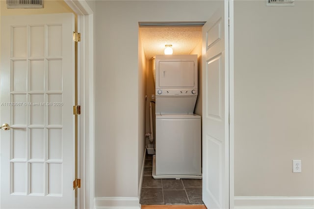clothes washing area featuring laundry area, a textured ceiling, tile patterned flooring, stacked washing maching and dryer, and baseboards