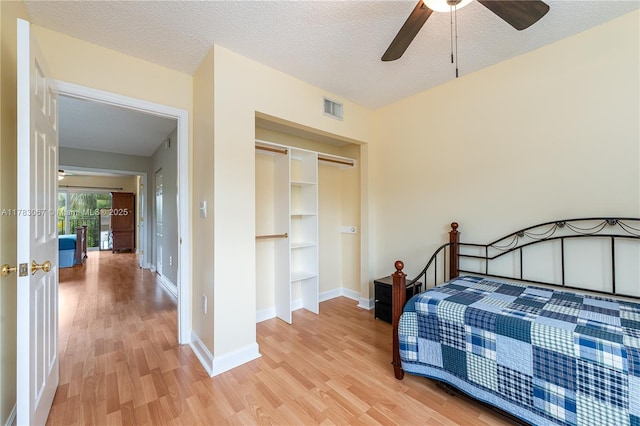 bedroom with light wood-style floors, visible vents, baseboards, and a textured ceiling