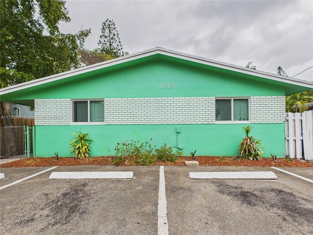 view of property exterior featuring brick siding, uncovered parking, and fence