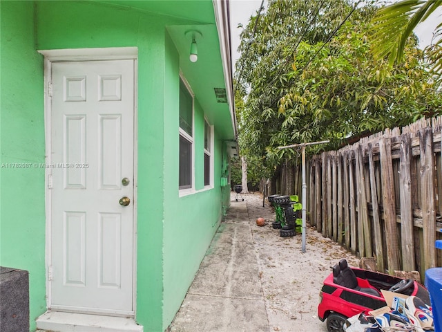view of exterior entry featuring stucco siding and fence