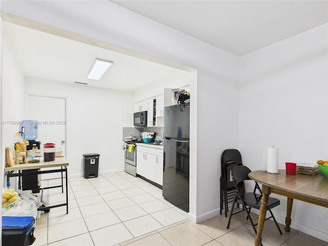 kitchen with white cabinets, baseboards, light tile patterned flooring, and black appliances