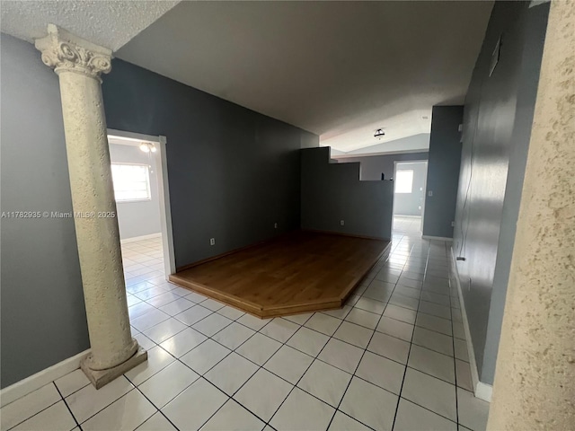 spare room featuring ornate columns, light tile patterned floors, baseboards, and lofted ceiling