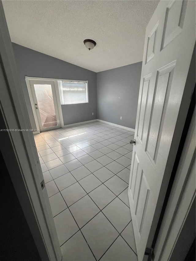 unfurnished room featuring light tile patterned floors, baseboards, vaulted ceiling, and a textured ceiling