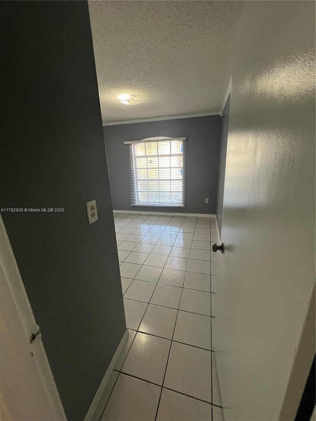 spare room with crown molding, light tile patterned floors, baseboards, and a textured ceiling
