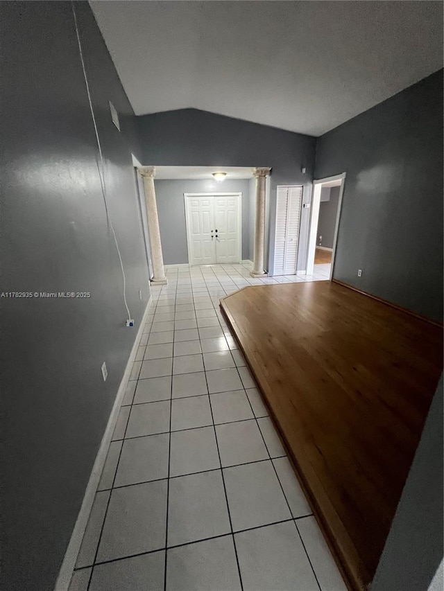 hallway featuring ornate columns, light tile patterned floors, baseboards, and vaulted ceiling