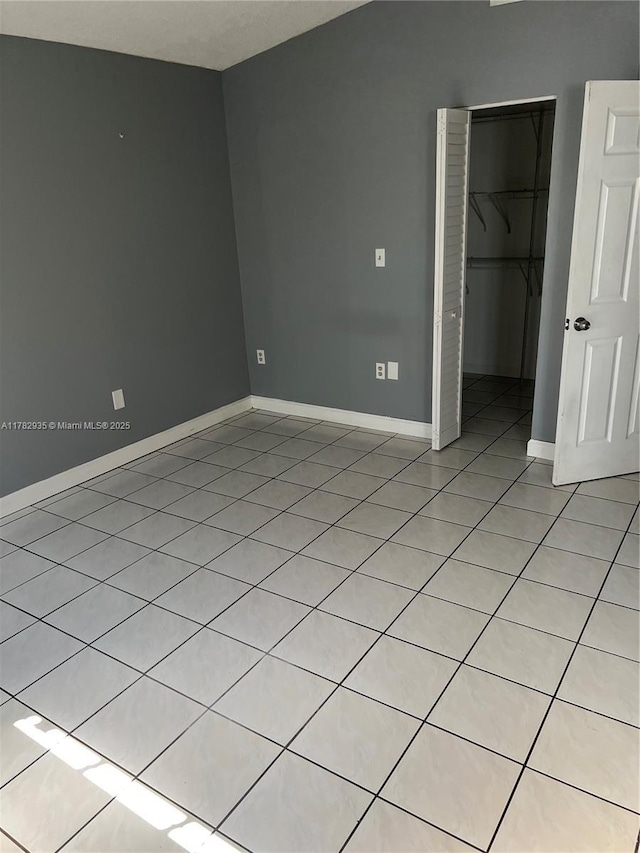 unfurnished bedroom with a closet, baseboards, a walk in closet, and light tile patterned floors