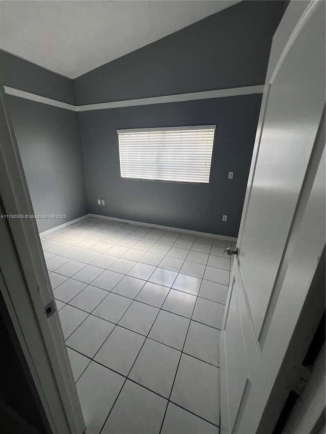 empty room with light tile patterned floors, baseboards, and vaulted ceiling