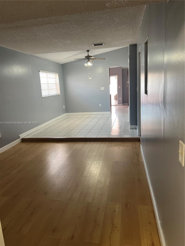 unfurnished room with a textured ceiling, a ceiling fan, visible vents, wood finished floors, and baseboards
