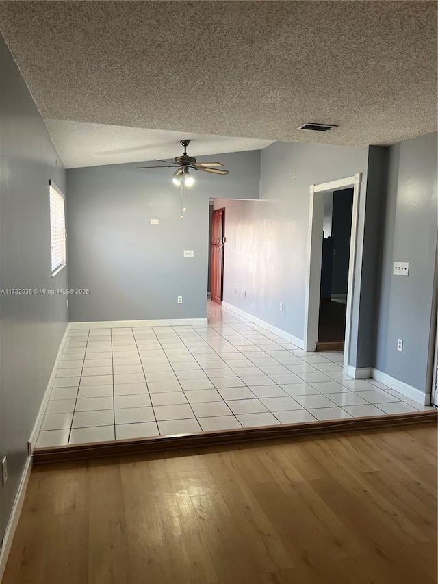 unfurnished room featuring visible vents, a ceiling fan, a textured ceiling, light wood-style flooring, and lofted ceiling