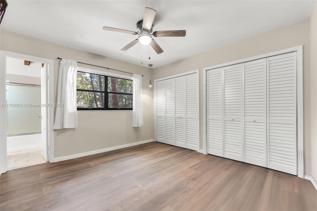 unfurnished bedroom with wood finished floors, baseboards, and multiple closets