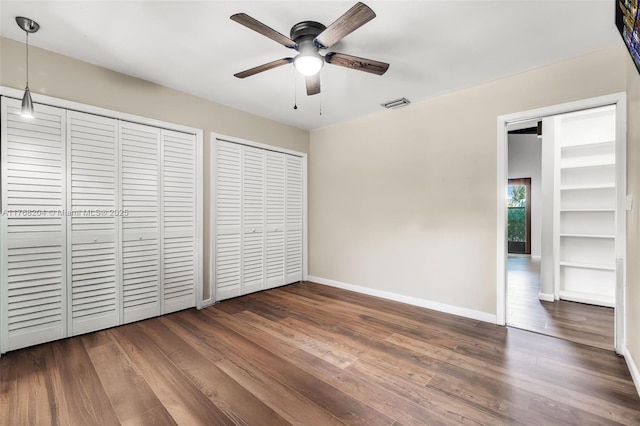 unfurnished bedroom with ceiling fan, visible vents, wood finished floors, multiple closets, and baseboards