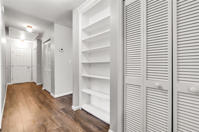 corridor featuring dark wood-type flooring, attic access, and baseboards