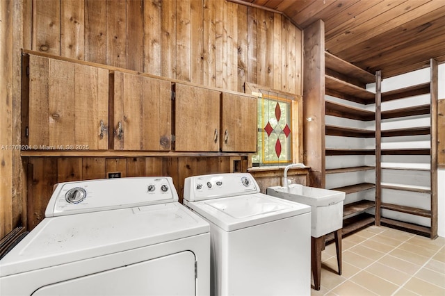 clothes washing area with light tile patterned floors, wooden ceiling, wooden walls, cabinet space, and washer and clothes dryer