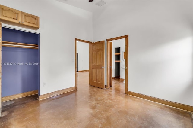 unfurnished bedroom featuring a closet, baseboards, a high ceiling, and finished concrete flooring