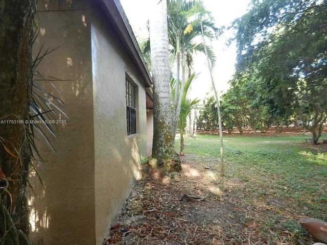 view of side of home with stucco siding and a yard