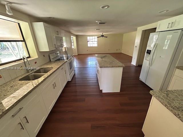 kitchen featuring a sink, light stone counters, open floor plan, white appliances, and dark wood-type flooring