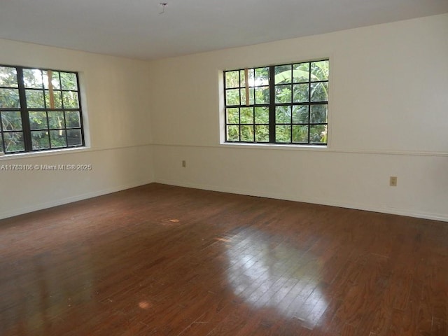 empty room with dark wood-style flooring, baseboards, and plenty of natural light