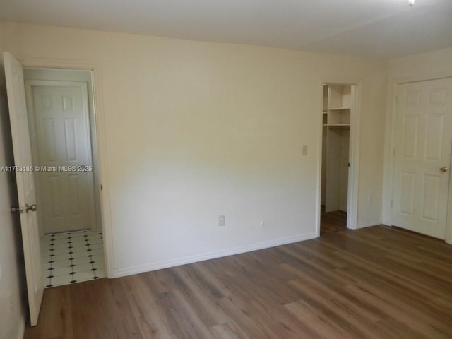 unfurnished bedroom featuring baseboards, a closet, wood finished floors, and a walk in closet