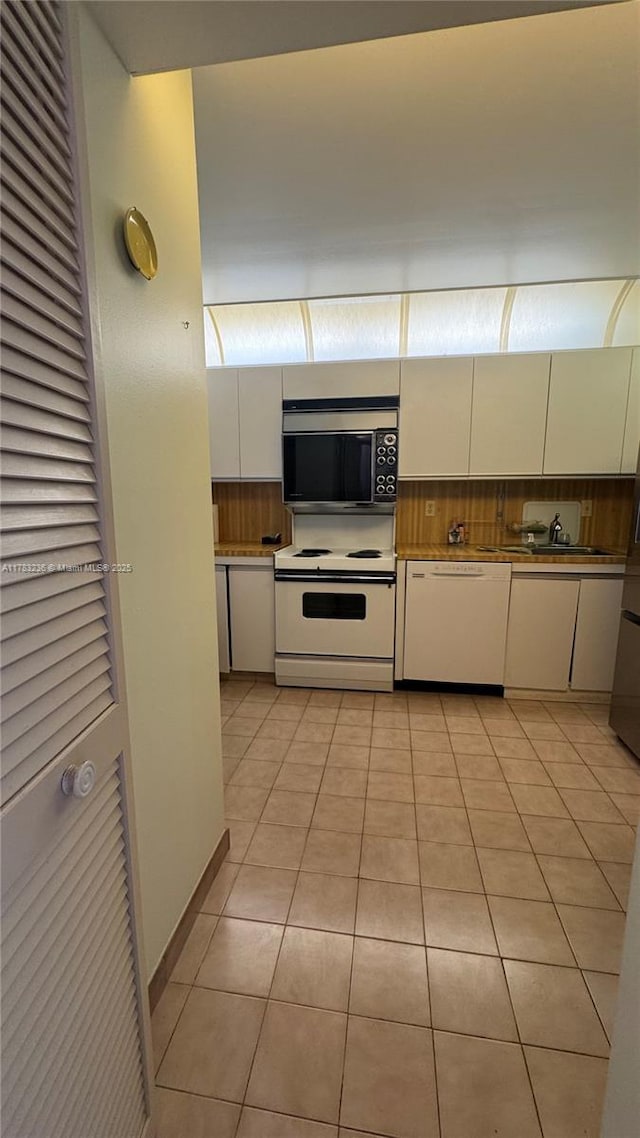 kitchen with backsplash, light tile patterned floors, white appliances, and white cabinets