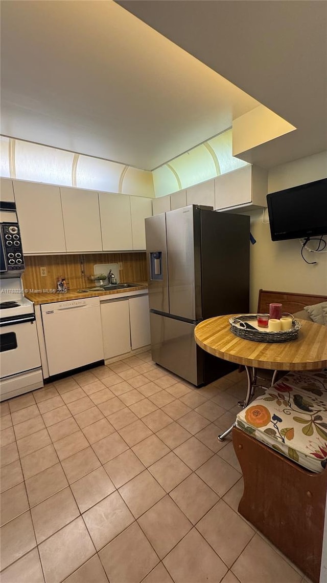 kitchen with light tile patterned floors, a sink, white appliances, and white cabinets