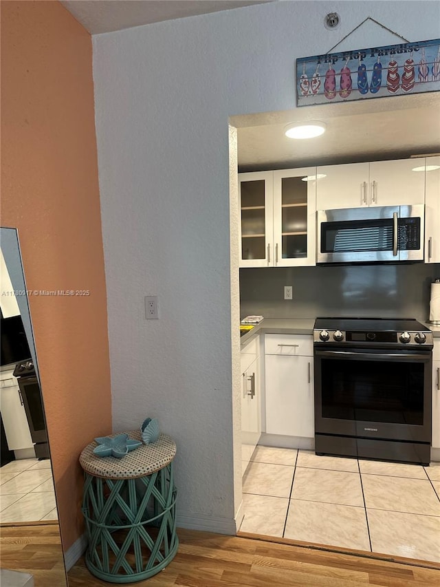 kitchen featuring glass insert cabinets, light wood-style flooring, white cabinets, appliances with stainless steel finishes, and light countertops