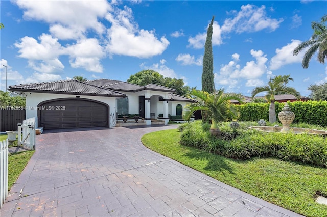 mediterranean / spanish home featuring an attached garage, a tile roof, fence, stucco siding, and decorative driveway
