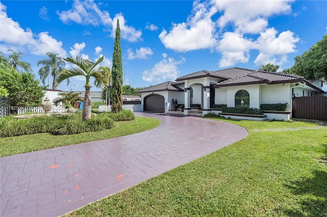 mediterranean / spanish-style house featuring curved driveway, an attached garage, a front yard, a tiled roof, and fence