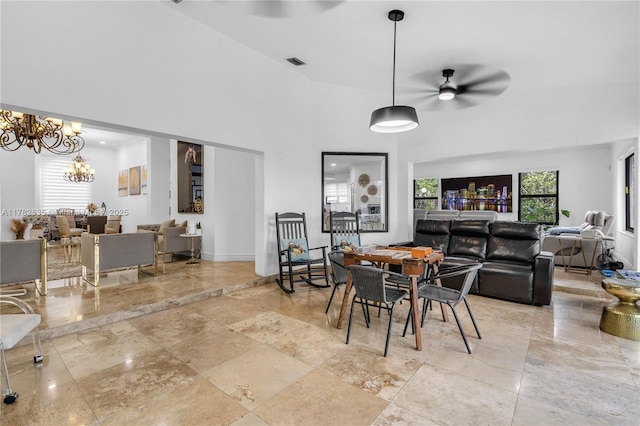 dining room featuring ceiling fan with notable chandelier, a towering ceiling, visible vents, baseboards, and stone tile flooring