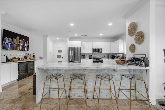 kitchen featuring crown molding, white cabinets, appliances with stainless steel finishes, light stone counters, and beverage cooler
