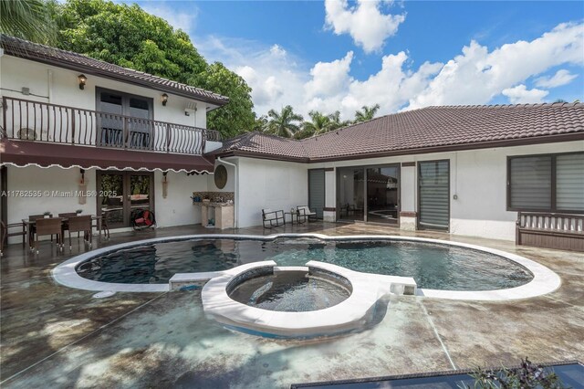 back of property with a balcony, stucco siding, a patio area, a pool with connected hot tub, and a tiled roof