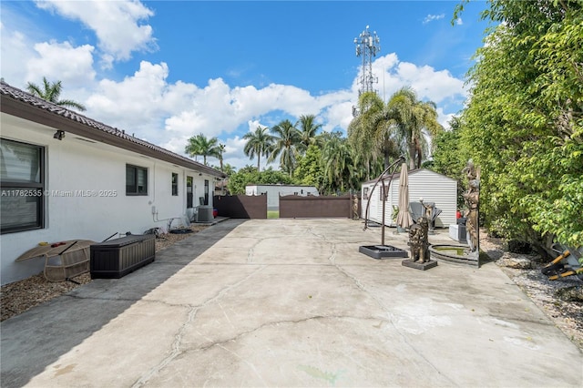 view of patio / terrace with central AC, fence, an outbuilding, and a storage unit