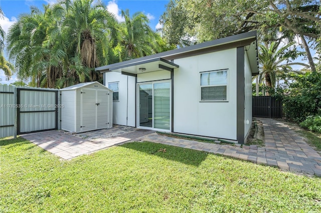 back of property featuring a yard, stucco siding, an outdoor structure, fence, and a gate
