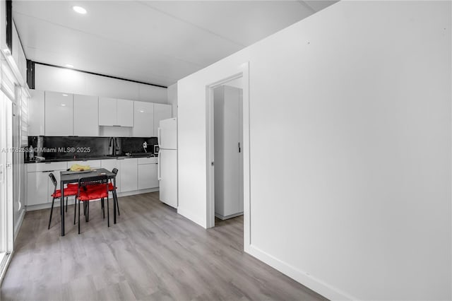 kitchen with tasteful backsplash, freestanding refrigerator, dark countertops, white cabinets, and light wood-style floors