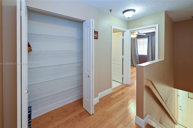 8390 NW 103rd St Unit 205H, Hialeah Gardens, FL 33016 - hallway featuring light wood-style flooring, a textured ceiling, baseboards, and an upstairs landing